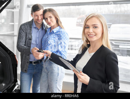 Autohändler, die Schlüssel zu den Kunden der Automobil-, Ordner. Happy hübsches Paar hinter, unter Tasten, lächelnd. Schöne blonde Frau an der Kamera schaut und posieren. Stockfoto