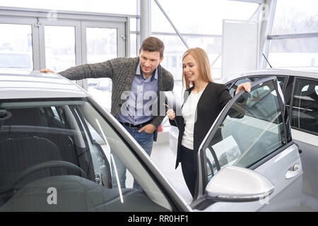 Weibliche Autohändler stehend mit Client der Händlerniederlassung im Showroom. Schöne Frau, um potenzielle Käufer Automobil, suchen Sie auf Auto Kabine mit Türen geöffnet. Manager arbeiten mit Kunden. Stockfoto
