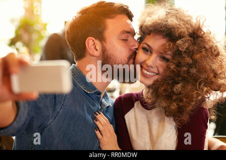 Curly girl mit Freund küssen während der Einnahme von selfie Stockfoto