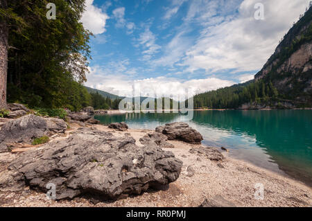 Der Pragser See, Italien. Blick vom Ufer auf das türkisfarbene Wasser. Blauer Himmel mit weißen Wolken. Rock im Vordergrund. Stockfoto