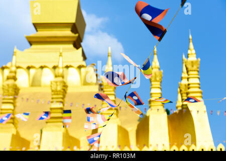 (Selektive Fokus) Einige Laos Fahnen schwenkten in den Vordergrund mit den unscharfen Pha That Luang im Hintergrund. Stockfoto