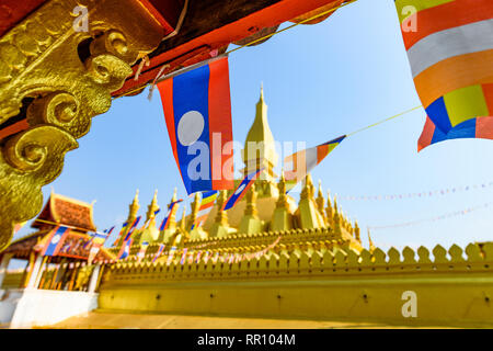 (Selektive Fokus) Einige Laos Fahnen schwenkten in den Vordergrund mit den unscharfen Pha That Luang im Hintergrund. Stockfoto