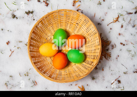 Fünf bunte Ostereier in einem Strohkorb auf Schnee und Gras isoliert Ostereiersuche Stockfoto