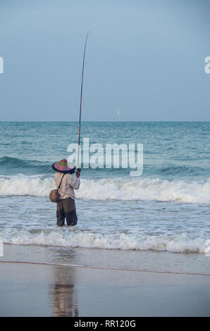 Lone Fischer tragen eine kegelförmige Hut Angeln mit einer Rute aus der Strand von Jimbaran Bay Bali Indonesien. Stockfoto