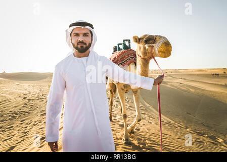 Stattlich im Nahen und Mittleren Osten Mann mit kandura und gatra reiten auf einem Kamel in der Wüste Stockfoto