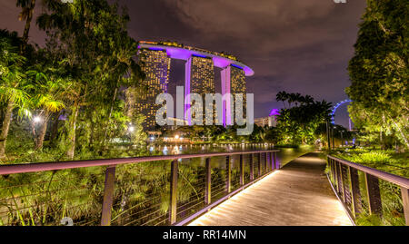 Holzweg am Dragonfly Pond in Gardens The Bay bei Nacht mit dem Marina Bay Sands Hotel im Hintergrund, Singapur Stockfoto