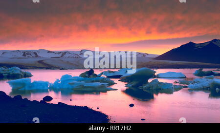 Schwimmende Eisberge auf dem Gletschersee Jökulsárlón Gletscherlagune mit schwarzem Sand Strand im Vordergrund und Gletscher und Roter Himmel bei Sonnenuntergang im Hintergrund, Island. Stockfoto