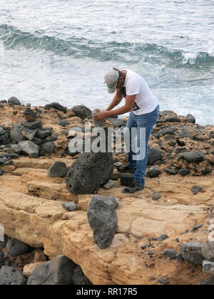 Mann an der Küste von Playa Blanca erstellen Rock Art Statuen von balancing Steine: Künstlerische Kreativität oder Zerstörung des Ökosystems? Stockfoto