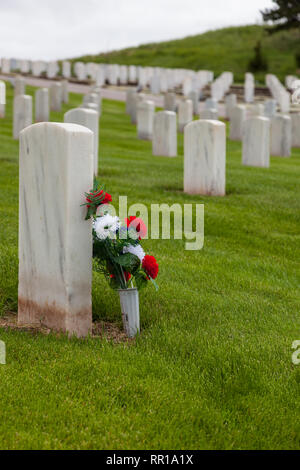 Eine Gruppe von Rot Weiß und Blau Blumen gegen eine Marmor Grabstein in einem militärischen Friedhof mit lebendigen Frühling Gras an einem Hang gelehnt. Stockfoto