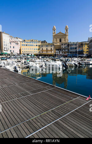 Holzsteg mit Blick auf Boote, die im Alten Hafen (Vieux Port) vor Anker liegen, mit der Saint-Jean-Baptiste-Kirche im Hintergrund, Bastia, Korsika, Frankreich. Stockfoto