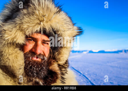 Bärtiger Mann braucht mehr als Gesichtsbehaarung zu halten in der kanadischen Arktis warnen. Hier im Bild trägt einen Wolf Pelzmantel auf dem gefrorenen Cumberland Meer. Stockfoto