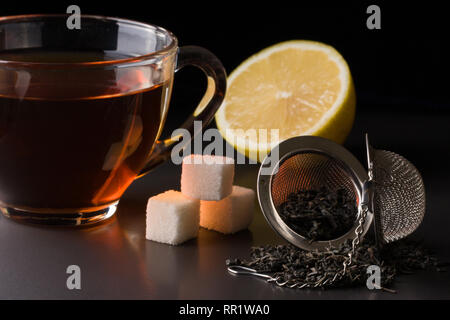 Tasse Tee mit einem Sieb und Zitrone auf dunklem Hintergrund Stockfoto