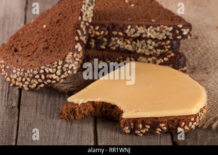 Scheiben Schwarzbrot mit Sesam und Käse auf dem alten Holz- Hintergrund Stockfoto