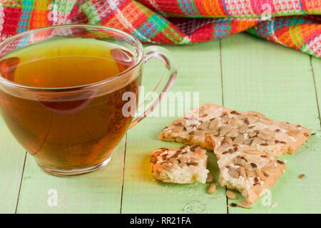 Knuspriges Brot mit Samen der Sonnenblumen, Flachs und Sesamsamen mit einer Tasse Tee auf einem grünen Holz- Hintergrund Stockfoto