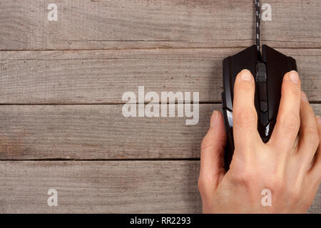 Schwarz Computer Maus mit einer Hand auf alten hölzernen Hintergrund mit Kopie Platz für Ihren Text. Ansicht von oben Stockfoto