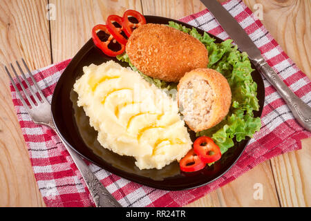 Zwei gebraten paniertes Schnitzel mit Kartoffelpüree und Salat auf einem schwarzen Schild Holz- Hintergrund Stockfoto