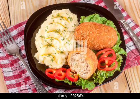 Zwei gebraten paniertes Schnitzel mit Kartoffelpüree und Salat auf einem schwarzen Schild Holz- Hintergrund Stockfoto