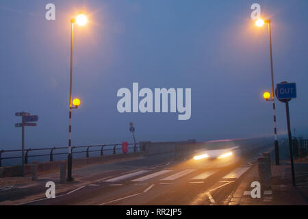 Southport, Merseyside. 24. Februar, 2019. UK Wetter. Diesig, neblig, Misty Start in den Tag mit leichtem Nieselregen wie am frühen Morgen Stadtzentrum Ampel die feuchten Fahrbahnen. Verkehr Trails von nächtlichen Partygängern mit Förderungsbedürftiger Taxis; als Lichter von vorbeifahrenden Fahrzeugen Reflexionen über die Fahrbahn verlassen. Credit: MWI/AlamyLiveNews. Stockfoto