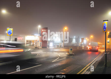 Southport, Merseyside. 24. Februar, 2019. UK Wetter. Diesig, neblig, Misty Start in den Tag mit leichtem Nieselregen wie am frühen Morgen Stadtzentrum Ampel die feuchten Fahrbahnen. Verkehr Trails von nächtlichen Partygängern mit Förderungsbedürftiger Taxis; als Lichter von vorbeifahrenden Fahrzeugen Reflexionen über die Fahrbahn verlassen. Credit: MWI/AlamyLiveNews. Stockfoto