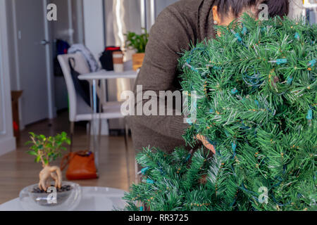 Frau hinter einem künstlichen Weihnachtsbaum, die Einrichtung der Ferienwohnung Deko von entwirren Niederlassungen Stockfoto