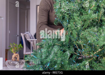 Frau hinter einem künstlichen Weihnachtsbaum, die Einrichtung der Ferienwohnung Deko von entwirren Niederlassungen Stockfoto