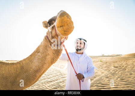 Stattlich im Nahen und Mittleren Osten Mann mit kandura und gatra reiten auf einem Kamel in der Wüste Stockfoto