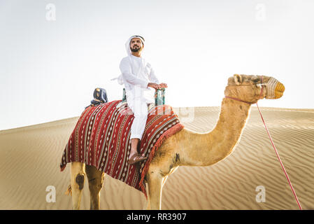 Stattlich im Nahen und Mittleren Osten Mann mit kandura und gatra reiten auf einem Kamel in der Wüste Stockfoto