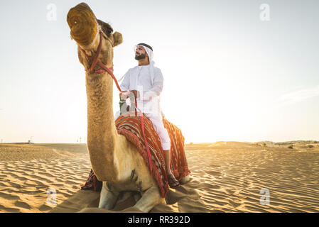 Stattlich im Nahen und Mittleren Osten Mann mit kandura und gatra reiten auf einem Kamel in der Wüste Stockfoto