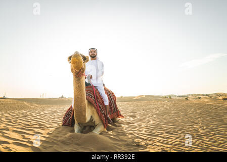 Stattlich im Nahen und Mittleren Osten Mann mit kandura und gatra reiten auf einem Kamel in der Wüste Stockfoto