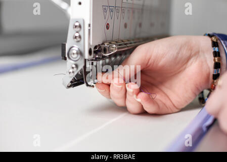 In der Nähe der weiblichen Händen abfüllen Thema in modernen Stickmaschine auf hellen Verschwommenes weiß Kopie Raum Hintergrund. Industrielle Stickerei, kommerzielle Produktion und qualitativ hochwertige Ergebnisse. Stockfoto