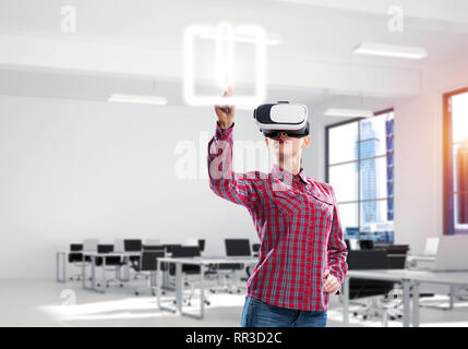 Frau in Casual tragen Virtuelle Realität Maske und berühren Sie das Symbol auf dem Bildschirm. Mixed Media Stockfoto