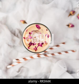 Eiskaffee mit Rose und Kardamom in ein hohes Glas mit getrockneten Rosen und Strohhalme auf weißer und grauer Seide Hintergrund umgeben. Ansicht von oben mit der Kopie Raum fo Stockfoto