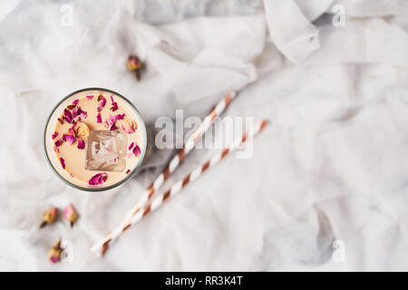 Eiskaffee mit Rose und Kardamom in ein hohes Glas mit getrockneten Rosen und Strohhalme auf weißer und grauer Seide Hintergrund umgeben. Ansicht von oben mit der Kopie Raum fo Stockfoto