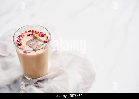 Eiskaffee mit Rose und Kardamom in ein hohes Glas auf weißer und grauer Seide Hintergrund. Kopieren Sie Platz für Text. Stockfoto