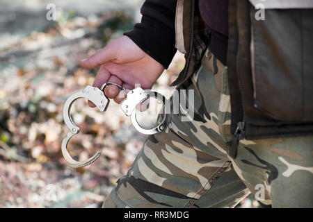 Der Mensch in der Tarnung ermüdet Holding Handschellen in seine Hand in ein Konzept der Strafverfolgungsbehörden angezeigt Stockfoto
