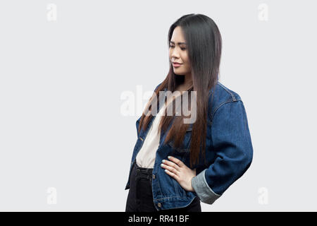 Spin oder Niere Schmerzen. Profil Seitenansicht Portrait von schöne Brünette asiatische junge Frau in lässigem Blue Denim Jacke ansehen und berühren Sie Zurück. st Stockfoto