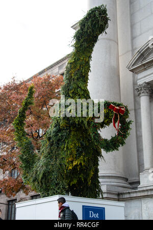 New York City, Vereinigte Staaten - 17. November 2018: eine Hecke Formgehölze geformt wie ein Dinosaurier Holding a Christmas Wreath außerhalb des American Museum der Natu Stockfoto