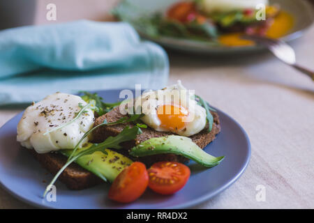 Sandwich mit Avocado, pochierte Eier, Rucola und Tomaten Stockfoto