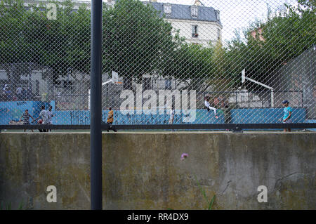 Kinder und Jugendliche spielen und hängen auf dem umzäunten Fußballplatz, Square Léon, Rue des Gardes, Goutte d'Or, 75018, Paris, Frankreich Stockfoto