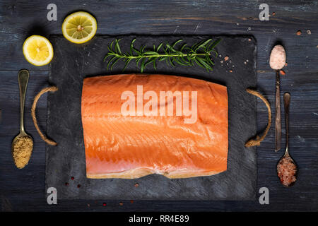 Roher Lachs filet auf schwarzem Schiefer Platte und Zutaten für die Herstellung von Graved Lachs. Salz, Zucker, Zitrone und Rosmarin im Hintergrund für trockene Heilung Marinade, da Stockfoto