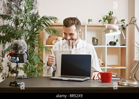 Ich kann es empfehlen! Fröhliche bärtigen Technologie Blogger zeigen auf neues Notebook, Daumen hoch und lächelte, während sie online Streaming Stockfoto
