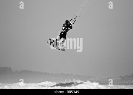 Ein Kite Surfer ist in die Luft in grauen bewölkten Wetter in Rhosneigr, Anglesey, North Wales, UK angehoben Stockfoto