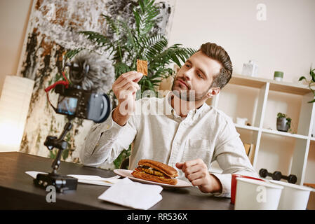 Sandwich Zutaten. Portrait der männlichen Bärtigen blogger Verkostung ein Lebensmittel während der Aufnahme neues Video für seine Vlog. Essen Konzept. Gastronomie Stockfoto