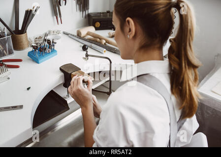 Auf Arbeit fokussiert. Seitenansicht des jungen weiblichen Juwelier einen Ring an ihrer Werkbank. Schmuck. Business. Schmuck Werkstatt. Close-up portra Stockfoto