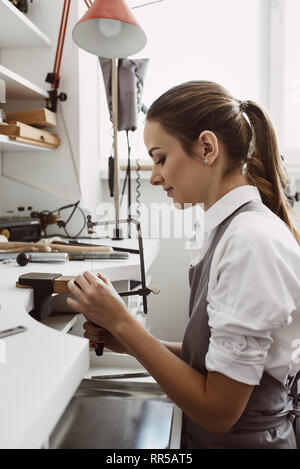 Auf einen Prozess konzentriert. Seitenansicht des jungen weiblichen Juwelier, neue Produkte in ihrem Schmuck Werkstatt. Schmuck. Business. Schmuck workshop Stockfoto