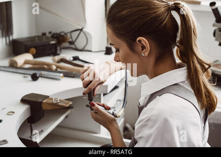 Nur einen Moment. Seitenansicht der weiblichen Juwelier Vorbereiten der Werkzeuge für die Arbeit mit den silbernen Ring an ihrem Schmuck Werkstatt. Schmuck. Business. Stockfoto