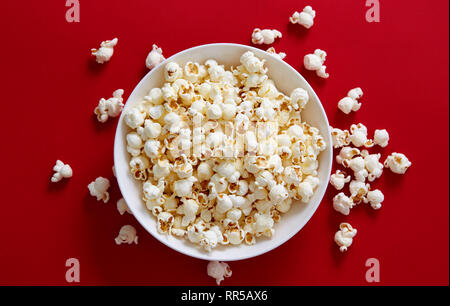 Popcorn in eine Schüssel geben. Direkt oberhalb der Schuß von Popcorn gegen den roten Hintergrund. Stockfoto