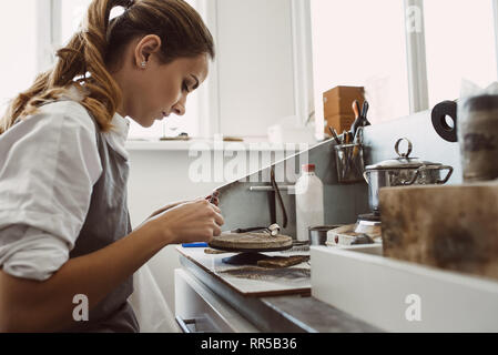 Geheime Technologie. Seitenansicht des jungen weiblichen Juwelier arbeiten an einer neuen Silber Ring an ihrer Werkbank. Schmuck. Arbeiten. Schmuck herstellerspez. Stockfoto