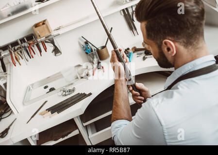 Das richtige Instrument. Rückansicht des jungen männlichen Juwelier Kontrolle ring Größe mit Spezialwerkzeug in der Werkstatt. Schmuck Werkstatt. Juwelier Tools Stockfoto