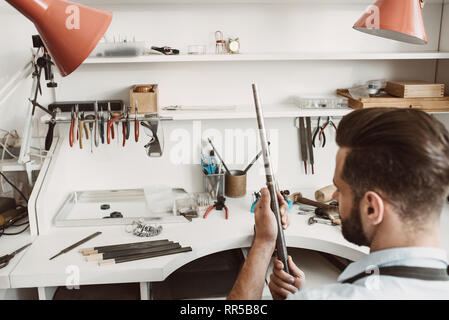 Perfekte Arbeitsplatz. Rückansicht des jungen männlichen Juwelier Kontrolle ring Größe mit Spezialwerkzeug in der Werkstatt. Schmuck Werkstatt. Juwelier Tools Stockfoto